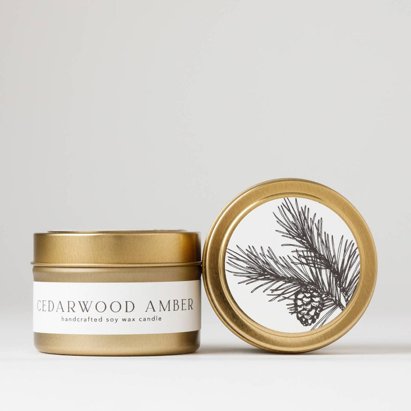 Cedarwood Amber candle with gold lid featuring a pine branch design on a light gray background