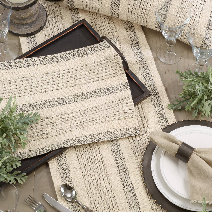 Elegant table setting with striped placemats, silverware, and candles on a wooden table.