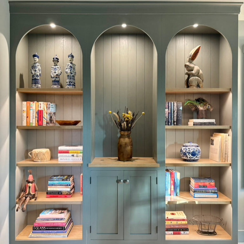 Gray bookshelf with arched shelves displaying books, decorative items, and a vase.
