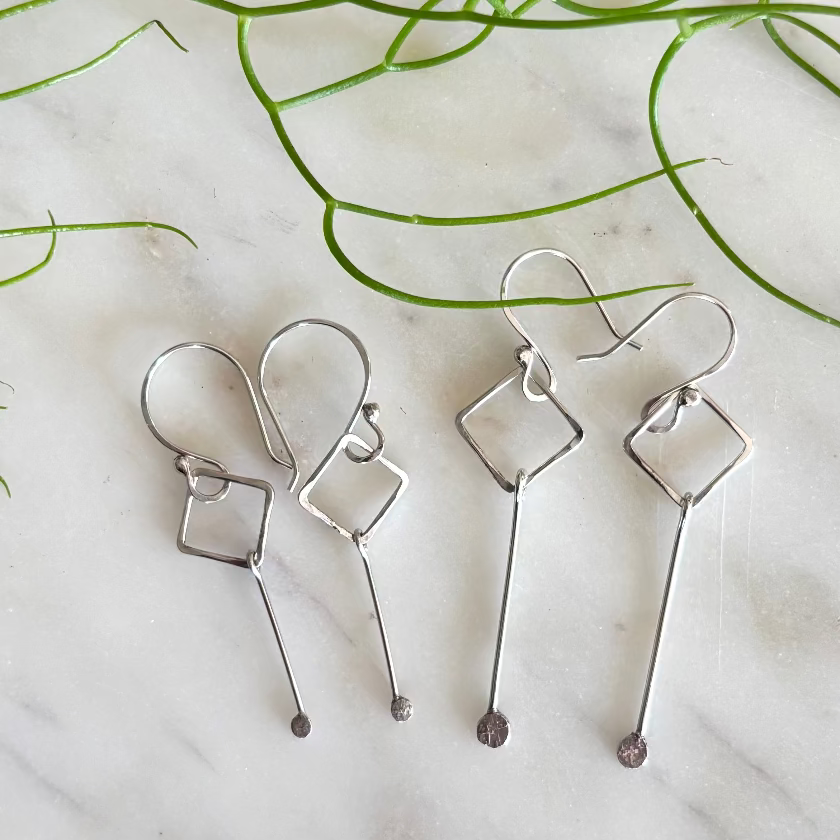 Pair of silver abstract earrings on a marble surface with green leaves.