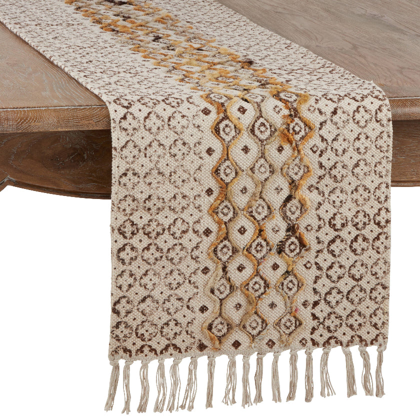 Patterned table runner with fringes on a wooden table