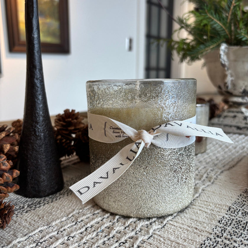Silver glittery candle with a ribbon on a textured surface, surrounded by decorative elements.