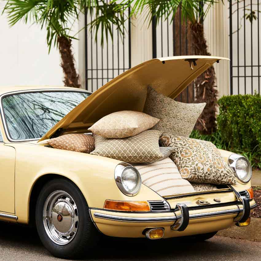 Vintage car with open hood filled with decorative pillows outdoors.