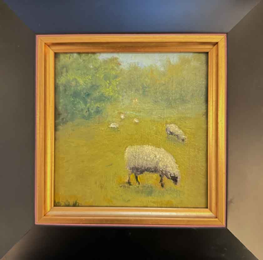 Framed painting of sheep in a field on a wall.