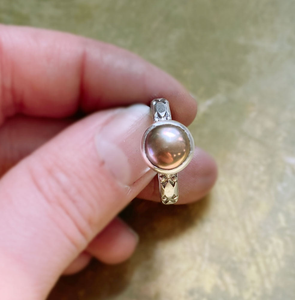 Silver ring with a large pearl held between fingers on a beige background