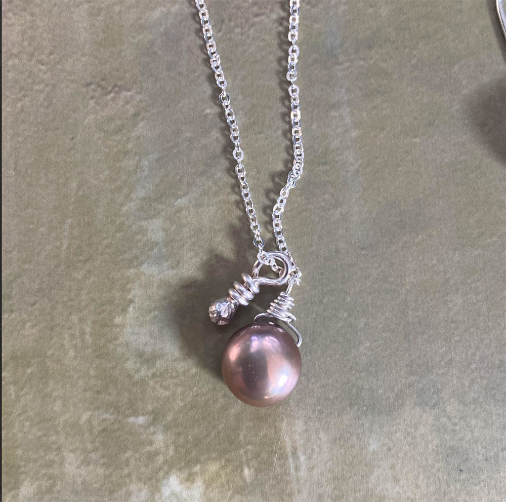 Necklace with a pink pearl pendant on a stone surface