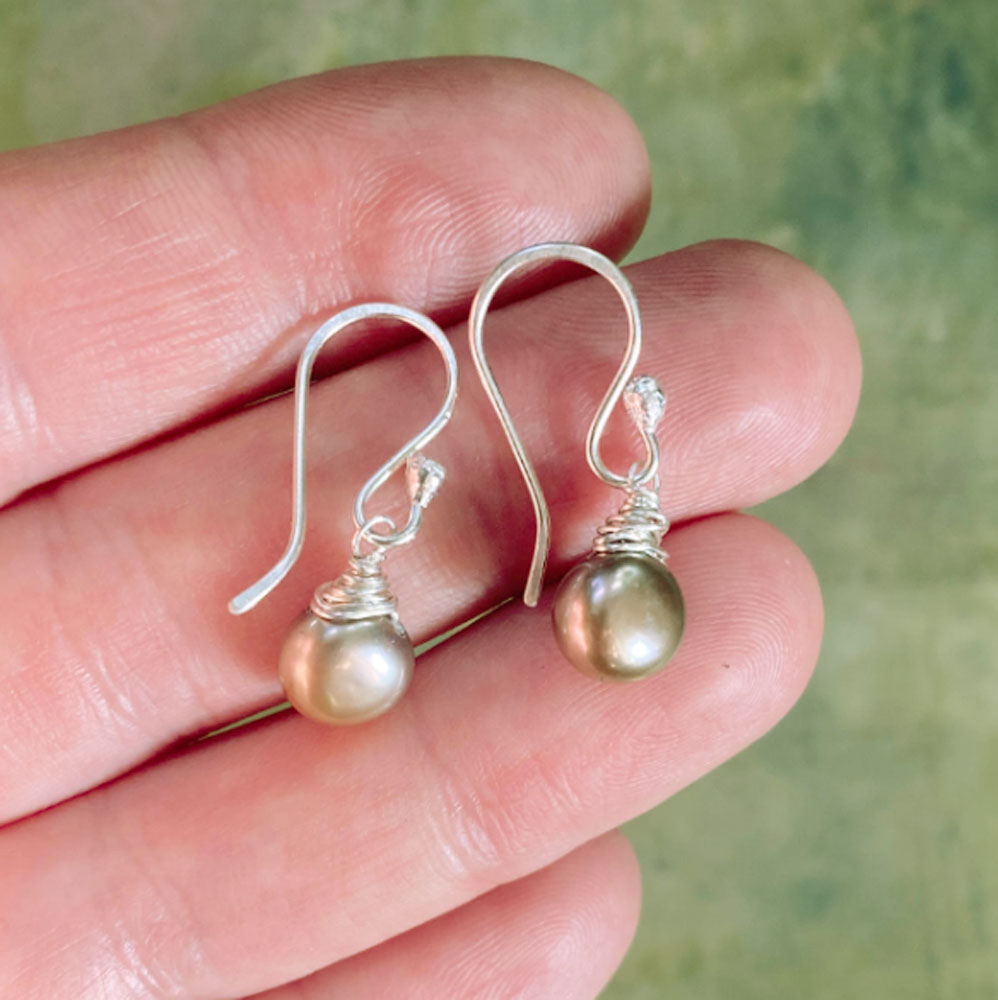 Gold pearl earrings held between fingers against a green background