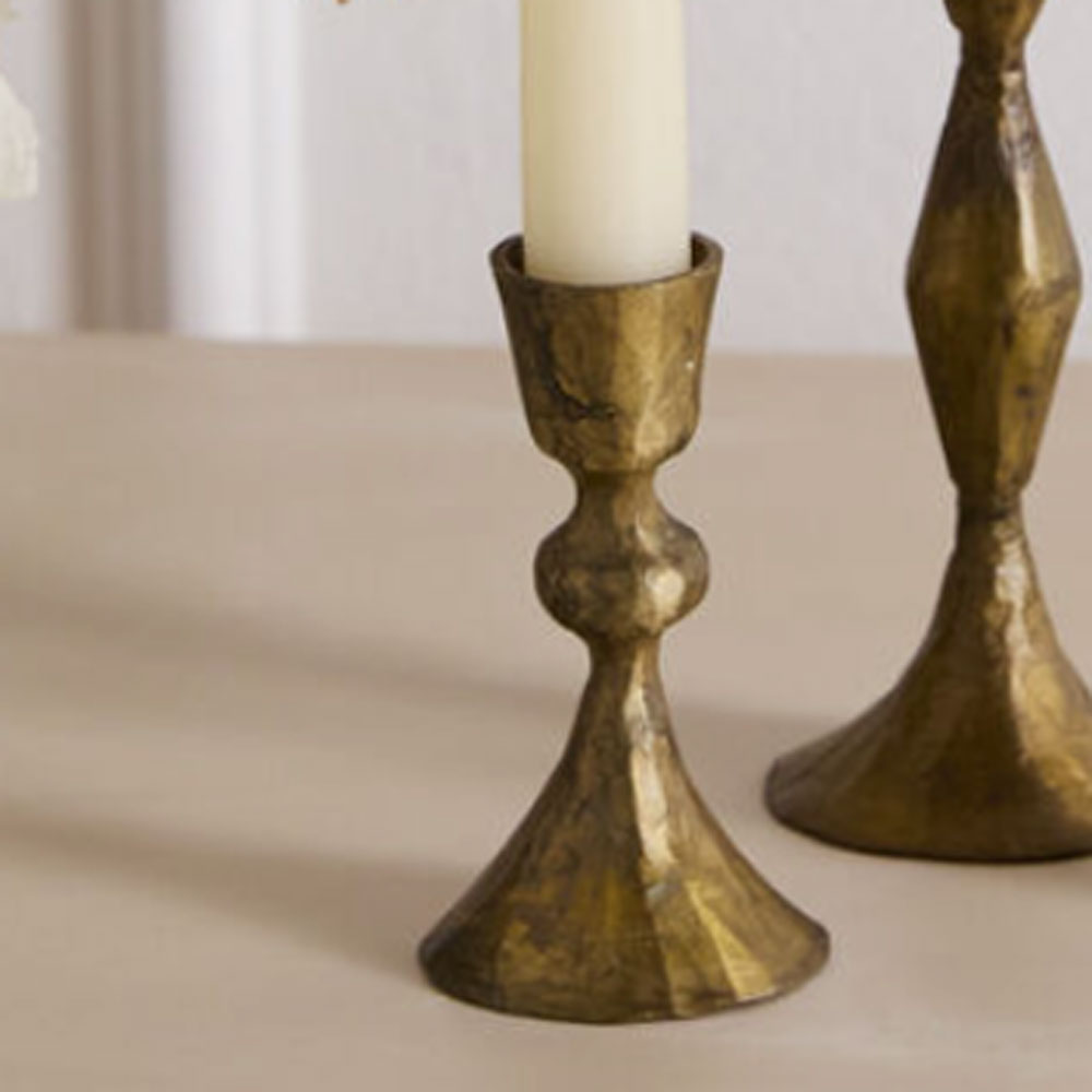 Two brass candle holders with candles on a beige surface