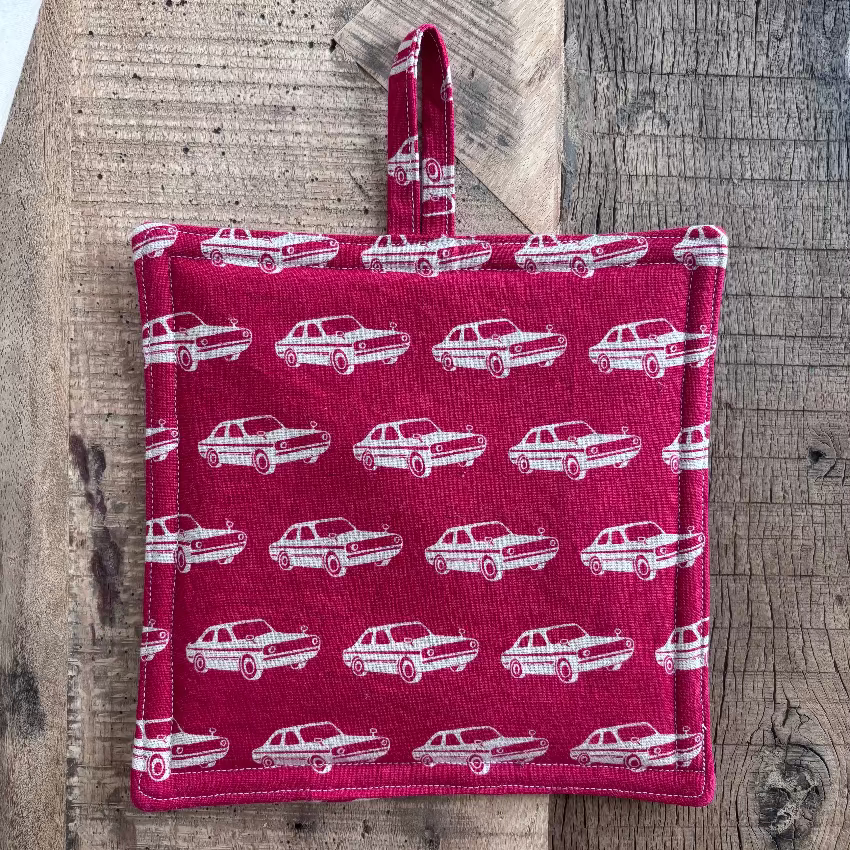 Red potholder with white car pattern on a wooden surface