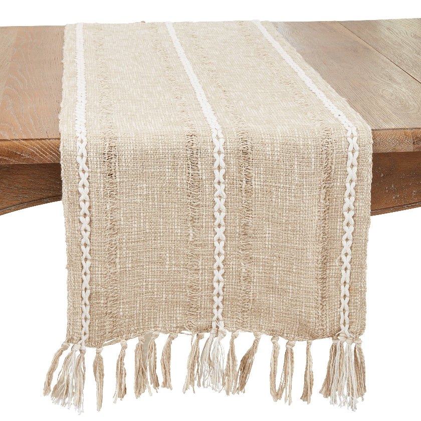 Beige woven table runner with white fringe on a wooden table.