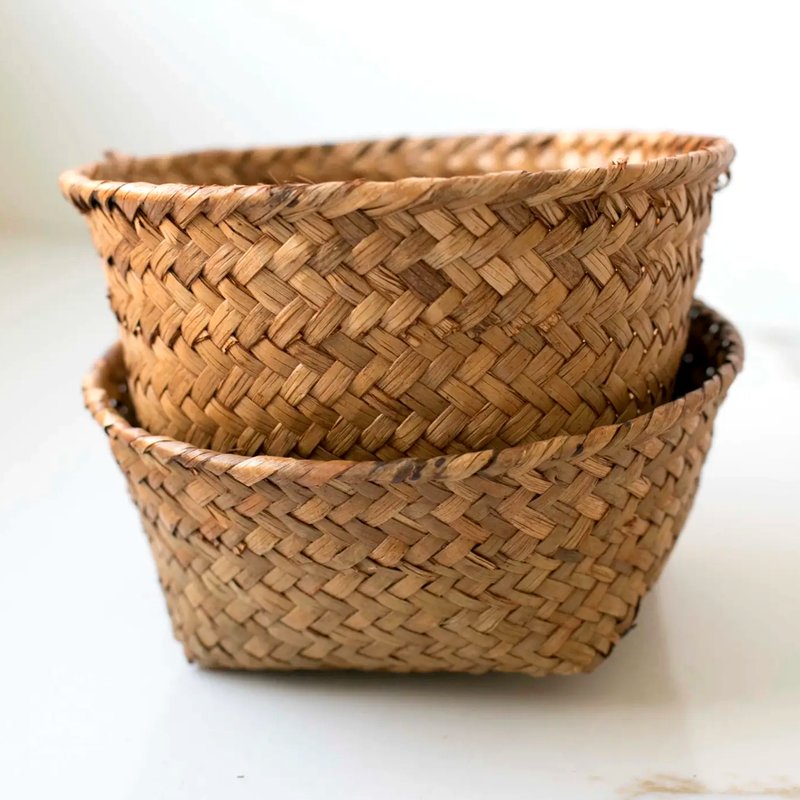 Two nested round woven baskets made from natural tan reed or straw fibers, photographed on a plain light background.