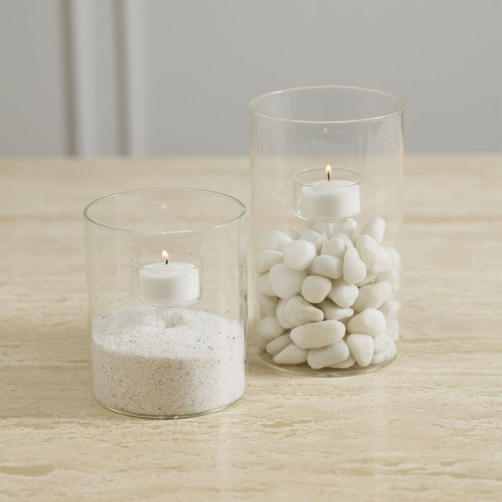 Two glass candle holders with candles on a wooden surface