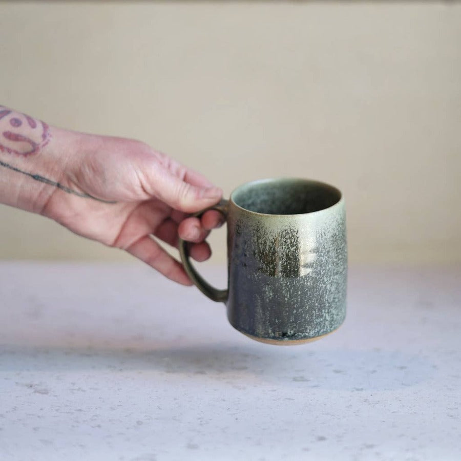 Gravesco Pottery moss green handmade stoneware mug held in hand, warm background