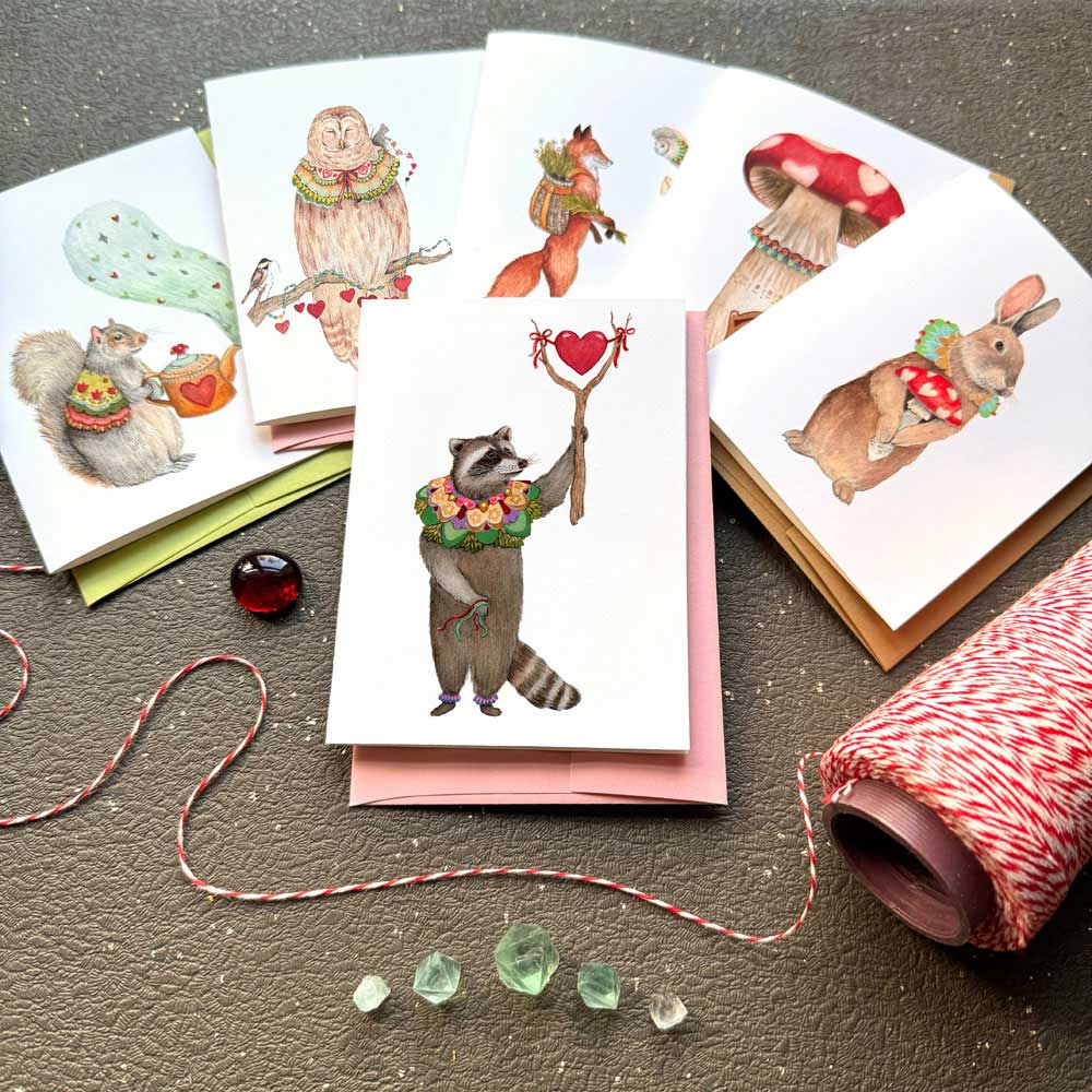 Set of greeting cards with animal illustrations on a textured surface with twine and stones.
