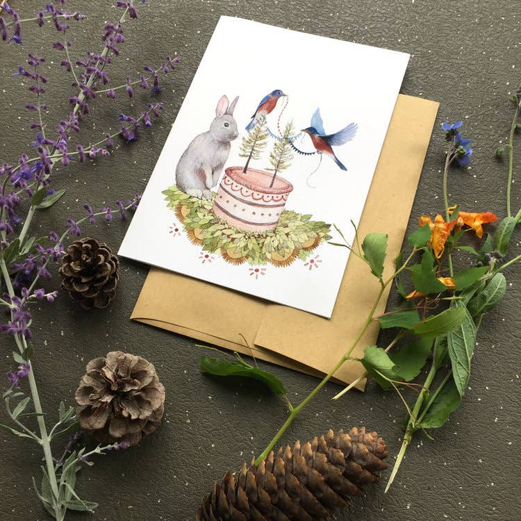 Polanshek of the Hills Celebrate illustrated greeting card featuring a rabbit and bluebirds around a woodland birthday cake, with kraft envelope