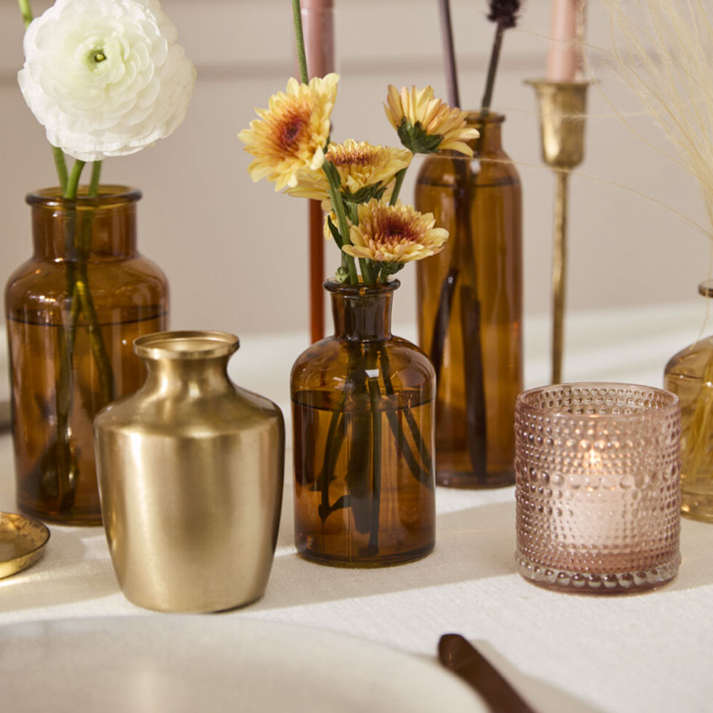 Decorative table setting with brown and gold vases, candles, and flowers.
