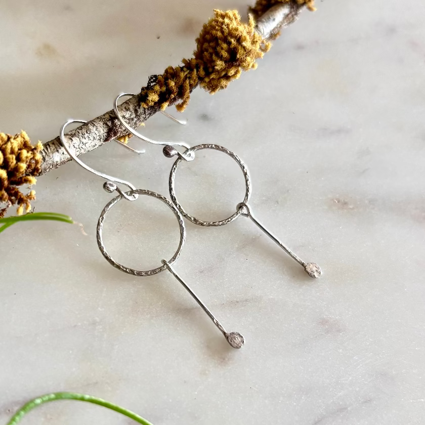 Silver hoop earrings on a branch with natural elements on a light background