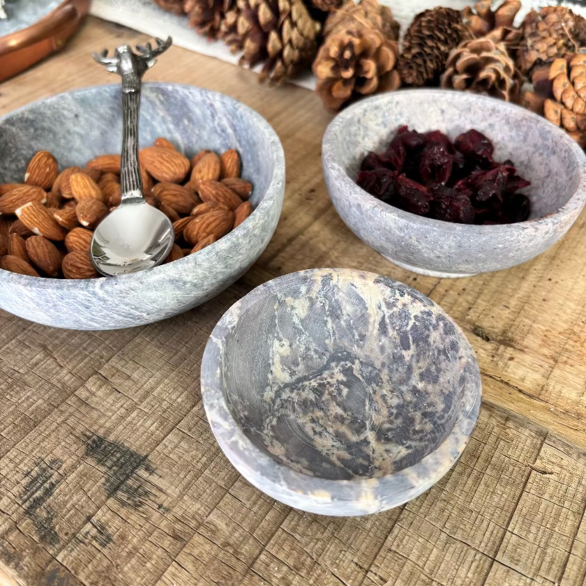 Three stone bowls containing almonds, dried fruit, and a spoon on a wooden surface.